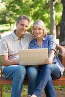 Couple with laptop sitting on bench