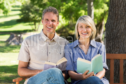 Couple reading books on bench in park