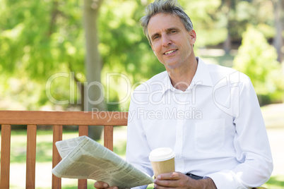 Businessman with disposable cup and newspaper in park