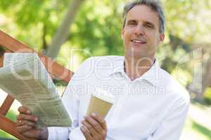 Businessman holding newspaper and coffee cup in park