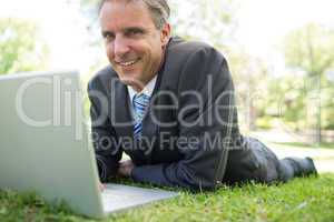 Businessman with laptop lying in park