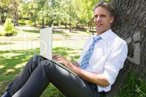 Businessman with laptop leaning on tree