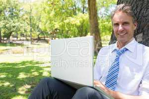 Businessman with laptop leaning on tree trunk