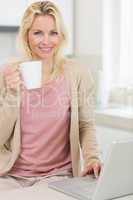 Beautiful woman with coffee cup using laptop in the kitchen