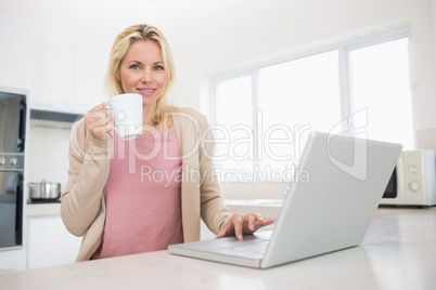 Portrait of beautiful woman with coffee cup using laptop in kitc