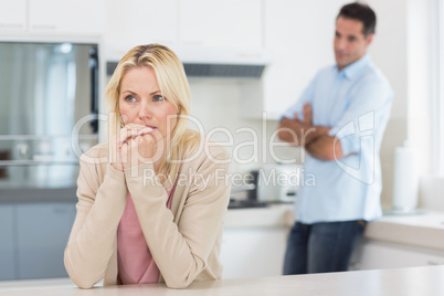 Thoughtful woman with blurred man in background in kitchen