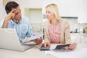 Worried couple with bills and laptop in kitchen