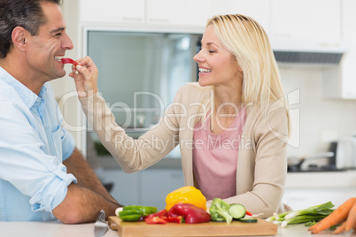 Happy loving woman feeding man vegetable in kitchen