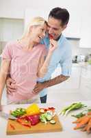 Happy loving woman feeding man vegetable in kitchen