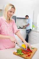 Woman chopping vegetables with man doing the dishes at kitchen