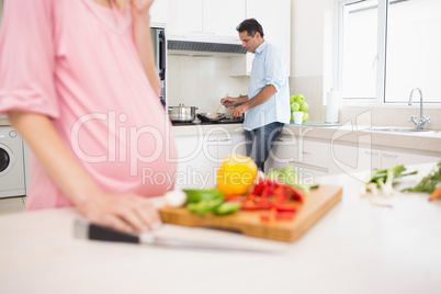 Mid section of woman chopping vegetables with man cooking food