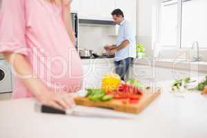 Mid section of woman chopping vegetables with man cooking food