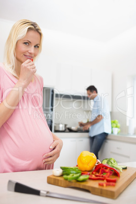 Pregnant woman with chopped vegetables and man cooking food