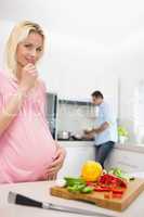 Pregnant woman with chopped vegetables and man cooking food