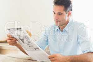 Serious casual man reading newspaper in kitchen