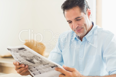 Smiling casual man reading newspaper in kitchen