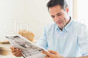 Smiling casual man reading newspaper in kitchen