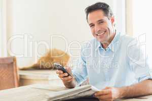 Smiling casual man with newspaper and cellphone in kitchen