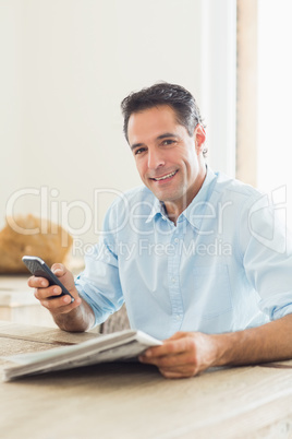 Smiling casual man with newspaper and cellphone in kitchen