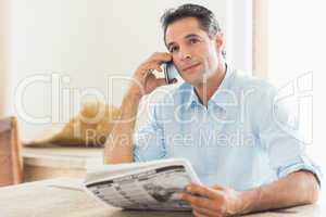 Man with newspaper using cellphone in kitchen