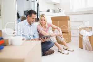 Couple using digital tablet amid boxes in house