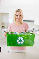 Smiling woman carrying recycling container in the kitchen