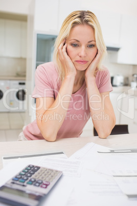 Worried woman with bills and calculator in kitchen