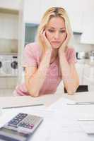 Worried woman with bills and calculator in kitchen