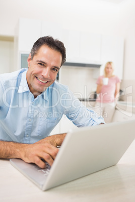 Man using laptop with woman drinking coffee at kitchen