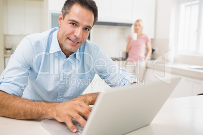 Man using laptop with woman drinking coffee at kitchen