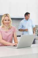 Woman using laptop with man drinking coffee in kitchen