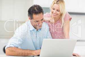 Happy couple using laptop in kitchen