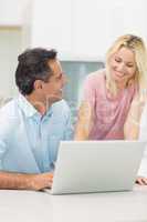 Happy couple using laptop in kitchen