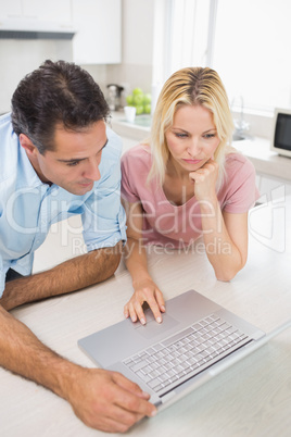 Concentrated couple using laptop in kitchen