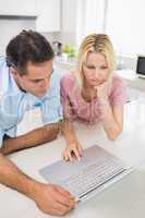 Concentrated couple using laptop in kitchen