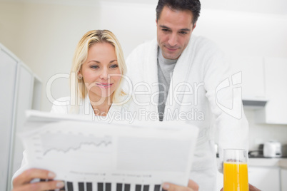 Couple in bathrobes reading newspaper in kitchen