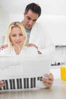 Couple in bathrobes reading newspaper in kitchen