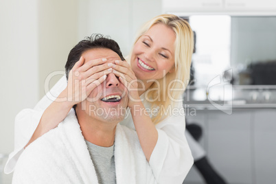 Smiling woman covering happy mans eyes in kitchen