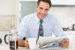 Smiling well dressed man with coffee cup and newspaper in kitche