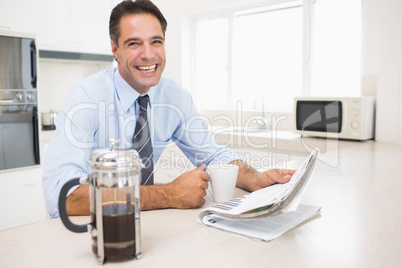Smiling well dressed man with coffee cup and newspaper in kitche