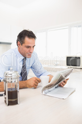 Well dressed man with coffee cup reading newspaper in kitchen