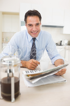 Smiling well dressed man with coffee cup and newspaper in kitche