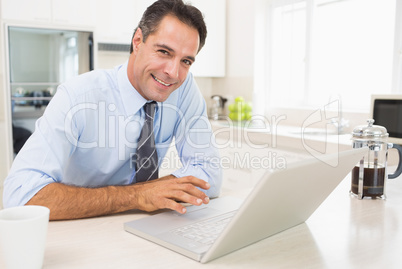 Smiling well dressed man using laptop in kitchen