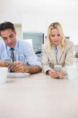 Well dressed couple text messaging in kitchen