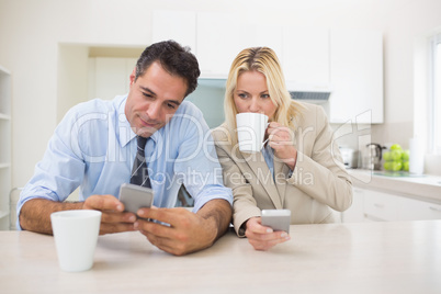 Well dressed couple with coffee cups text messaging in the kitch