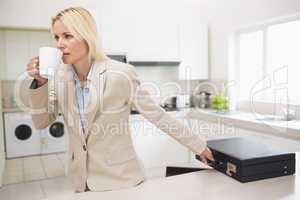 Well dressed woman drinking coffee while holding briefcase in ki