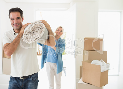 Smiling couple carrying rolled rug after moving in house
