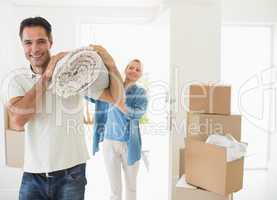 Smiling couple carrying rolled rug after moving in house