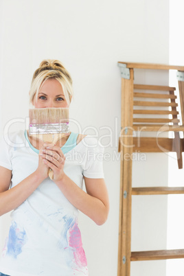 Woman holding paint brush in front of her face at new house