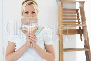 Woman holding paint brush in front of face at the new house